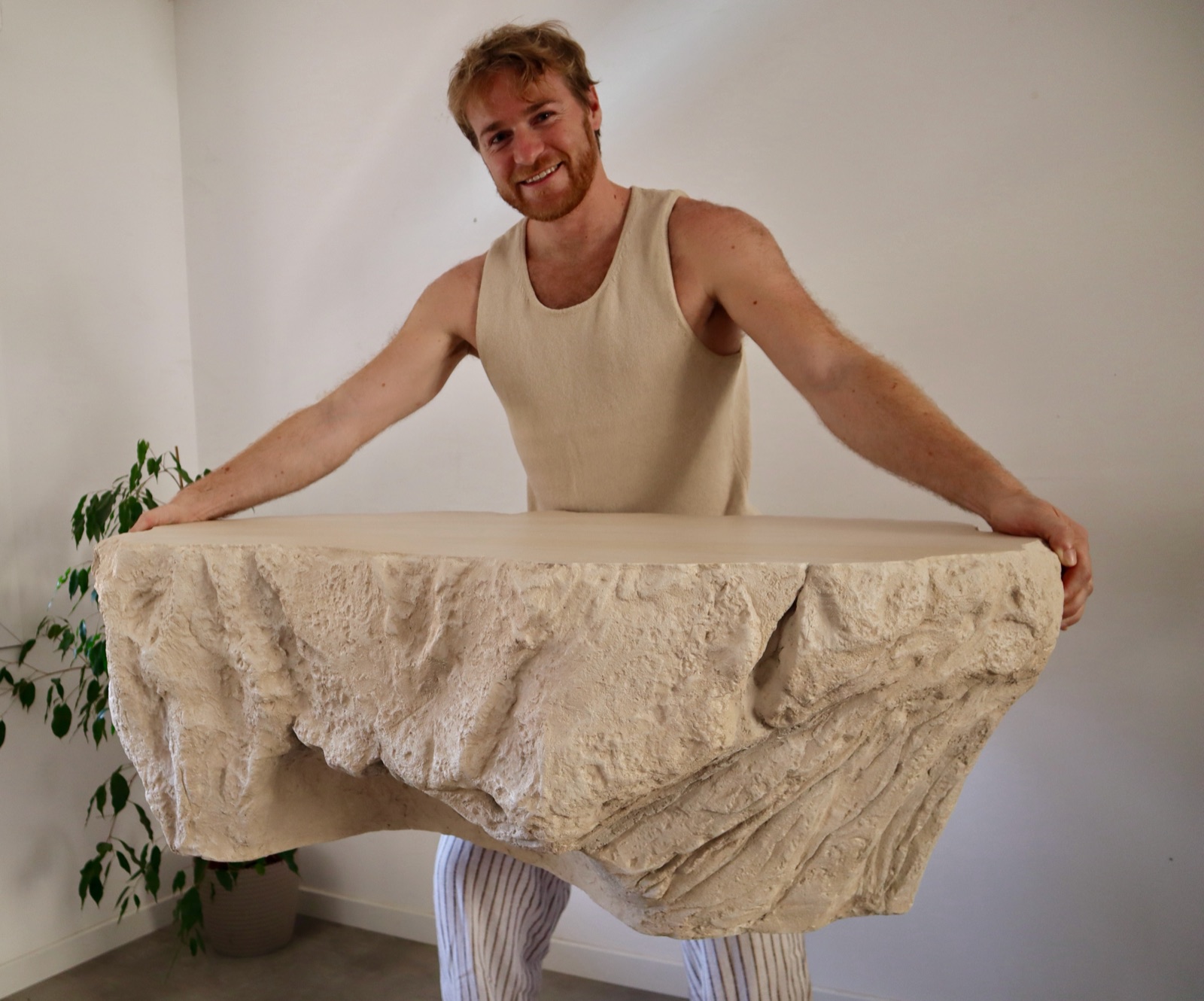 Louis Michel debout, tenant à bout de bras une table effet roche sculptée à la main